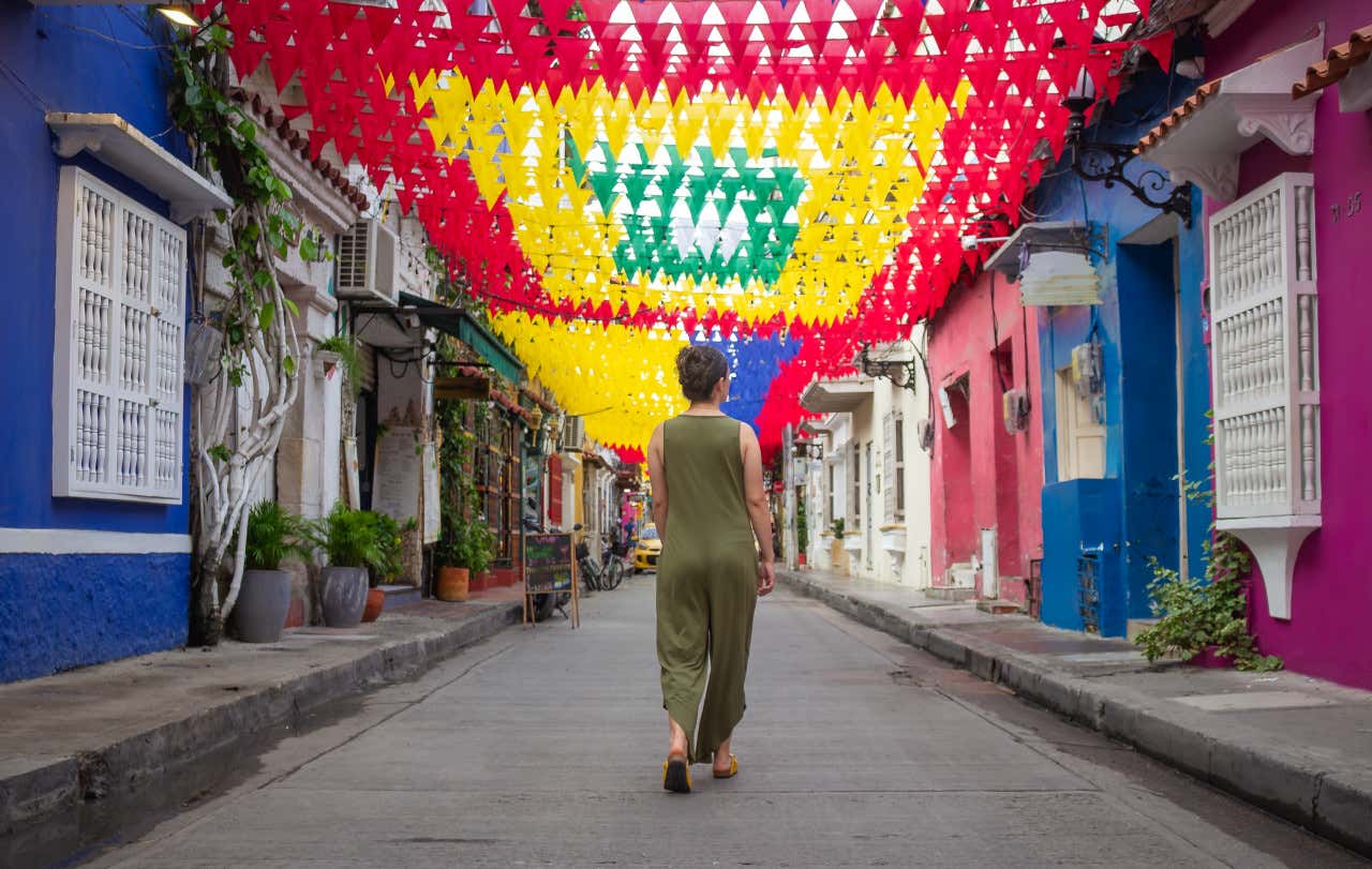 Una persona de espaldas caminando por una calle vacía con casas de colores en los laterales y banderines en lo alto