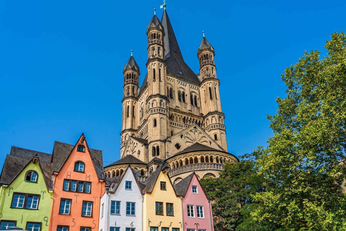 Torre de una iglesia románica frente a un conjunto de casas medievales de colores pastel en un día despejado