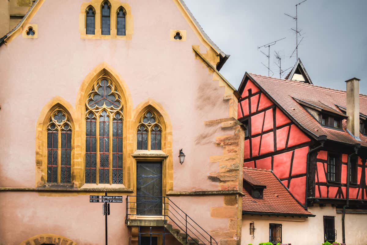 Una iglesia con vidrieras y una puerta con escaleras junto a una casa roa con vigas de madera descubiertas