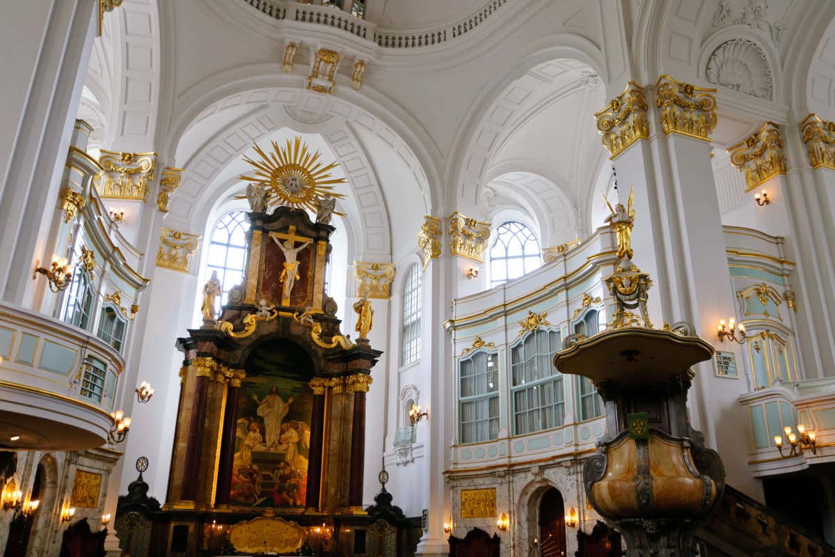Interior de una iglesia de Hamburgo con paredes y columnas blancas decoradas con pequeños detalles dorados