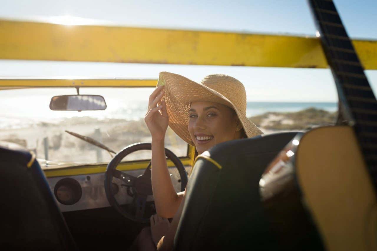 Una mujer sonríe a bordo de un coche con la vista al mar