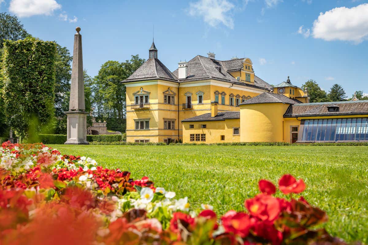 Fachada amarilla de un palacio de Salzburgo rodeado de césped, flores y un obelisco decorativo