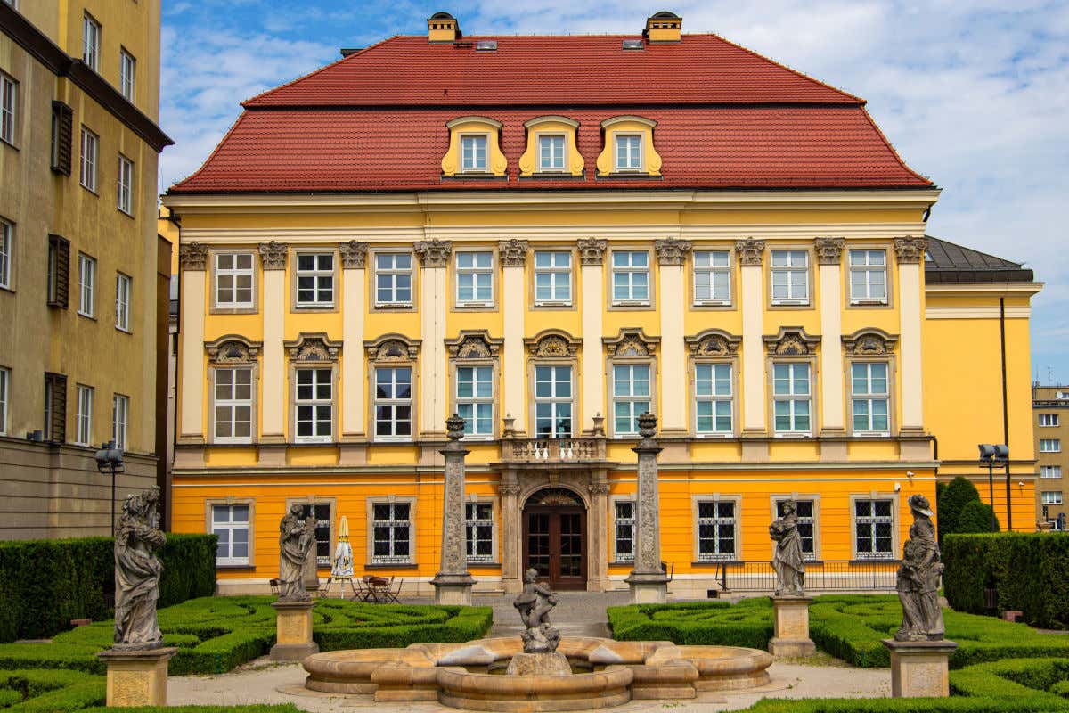 Fachada amarilla del Palacio Real de Breslavia frente a un jardín con esculturas