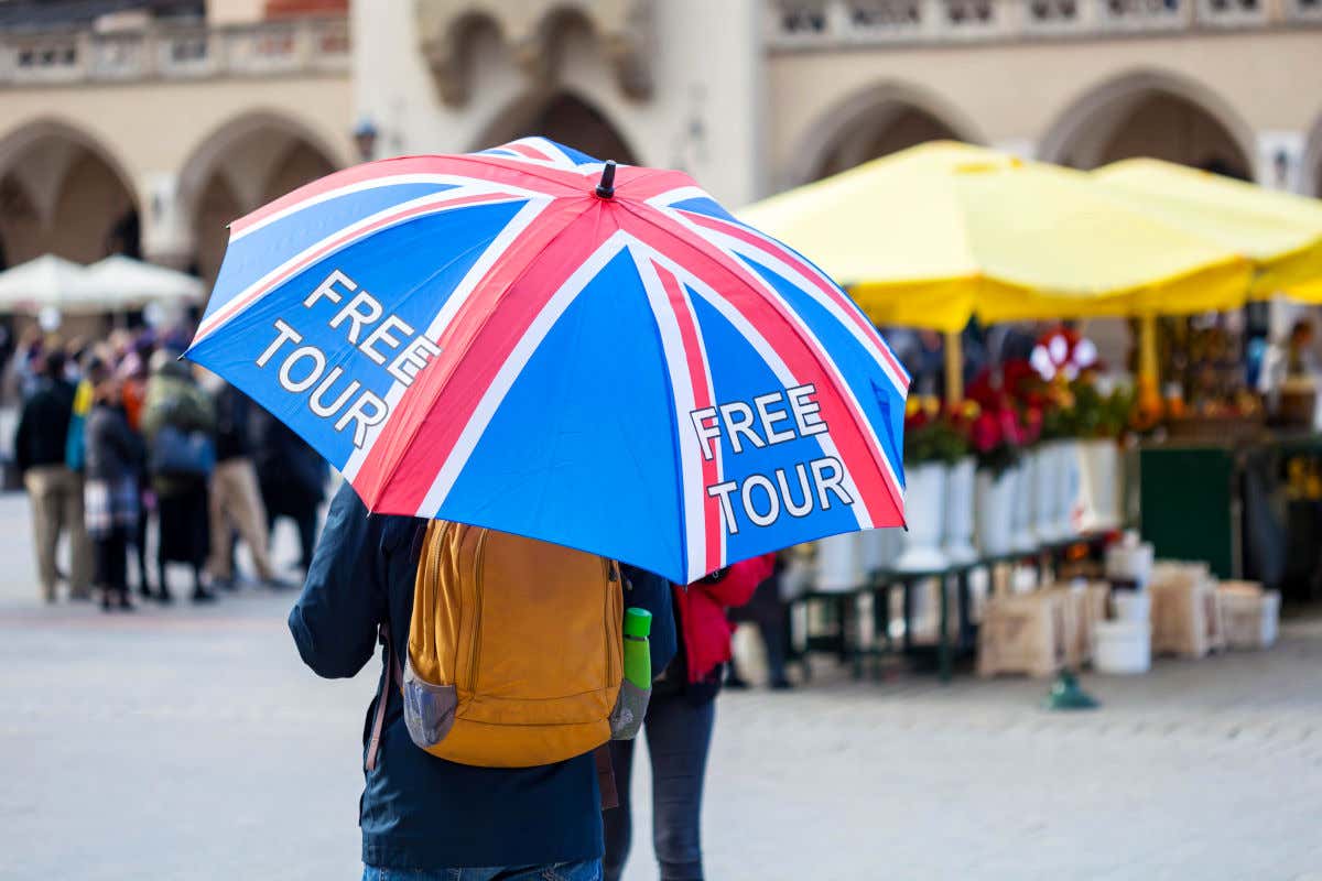Un guía de un free tour con un paraguas identificativo con las palabras 'Free tour' y la bandera británica en mitad de una plaza