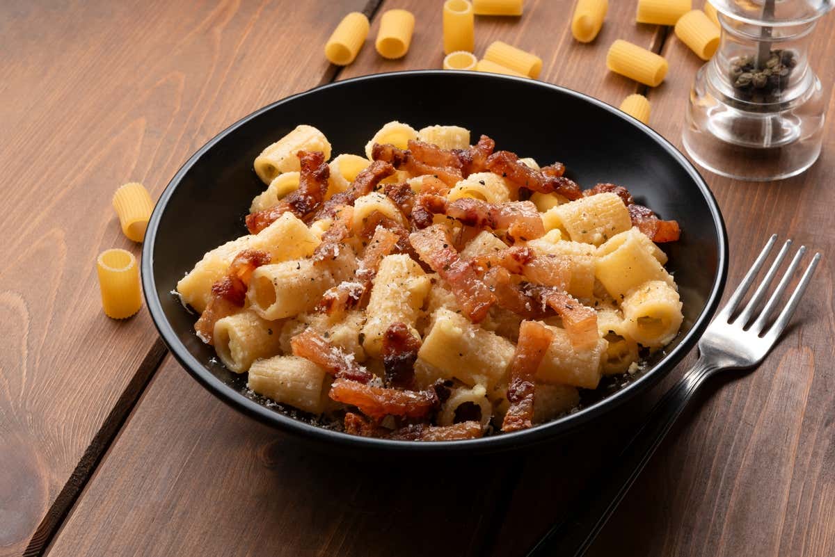 Plato de rigatoni a la carbonara sobre una mesa de madera