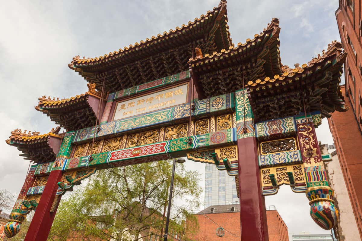 Puerta monumental de sobrecargada decoración, con dragones dorados y escritura china, indicando el inicio del Chinatown de Mánchester