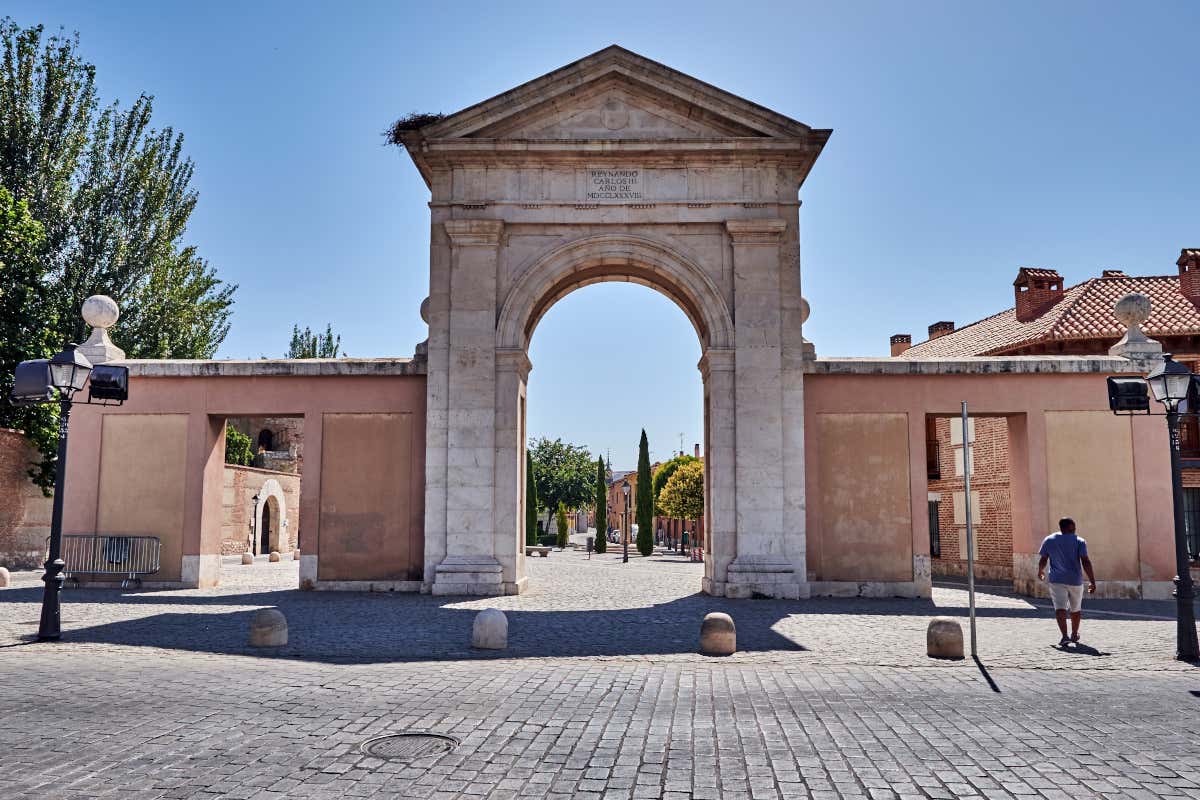 Un hombre paseando bajo los arcos de una antigua puerta monumental del siglo XVIII