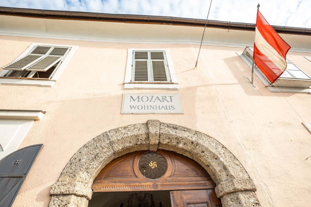 Fachada de un edificio antiguo con un cartel que indica que se trata de la casa de Mozart y con una bandera austríaca decorativa