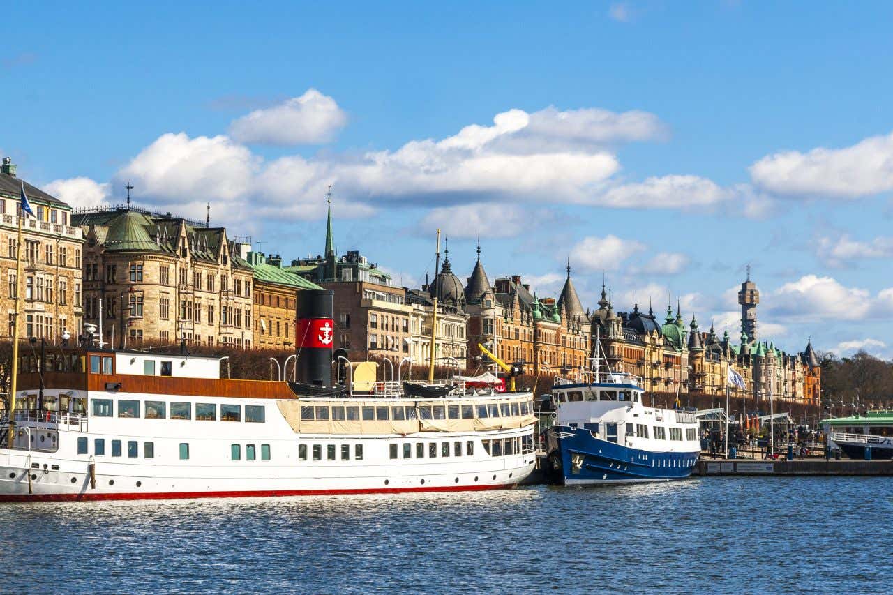 Alcune imbarcazioni ormeggiate davanti il centro storico di Stoccolma, fatto di palazzi antichi con alti pennacchi appuntiti, in una giornata di sole