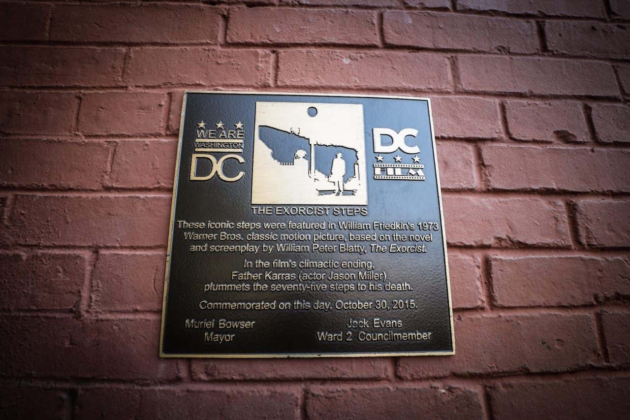 Uma placa em uma parede de tijolos indicando a localização da famosa Escadaria do Exorcista