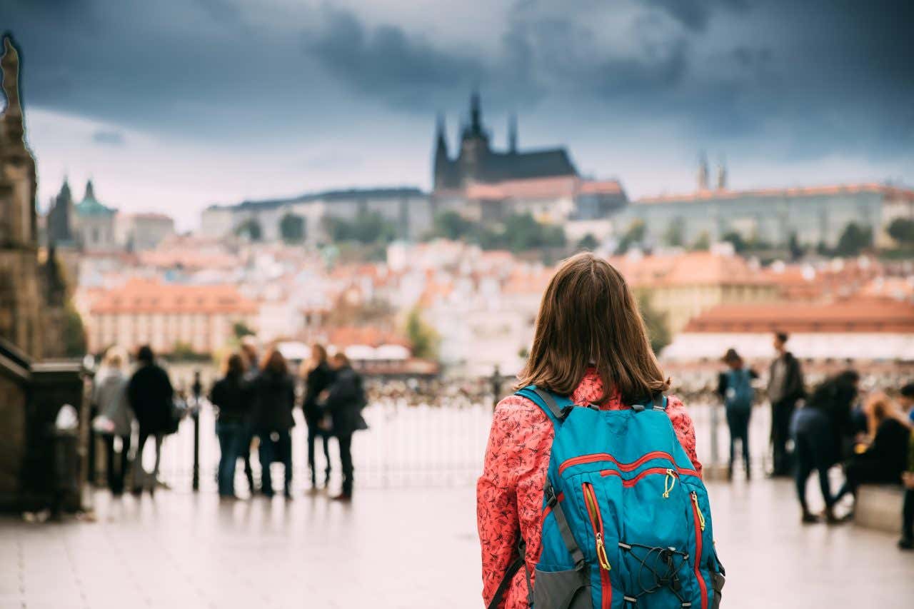 Una ragazza di spalle con uno zaino in spalla ammira il castello di Praga che si staglia all'orizzonte