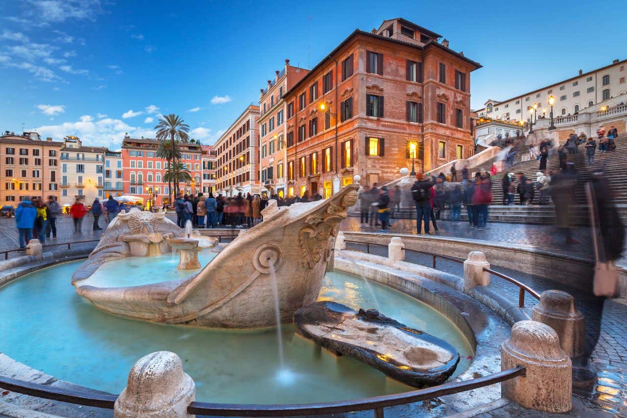 Fontana della Barcaccia di Pietro Bernini a Piazza di Spagna, scultura barocca a forma di barca semi-affondata con turisti sulla scalinata di Trinità dei Monti al crepuscolo