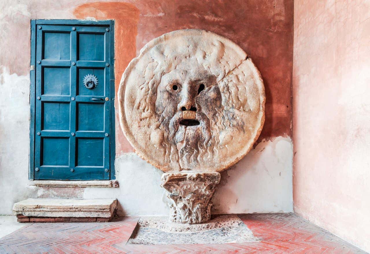 Antico mascherone romano in marmo della Bocca della Verità raffigurante un volto barbuto con bocca spalancata, murato verticalmente nel portico della Basilica medievale di Santa Maria in Cosmedin