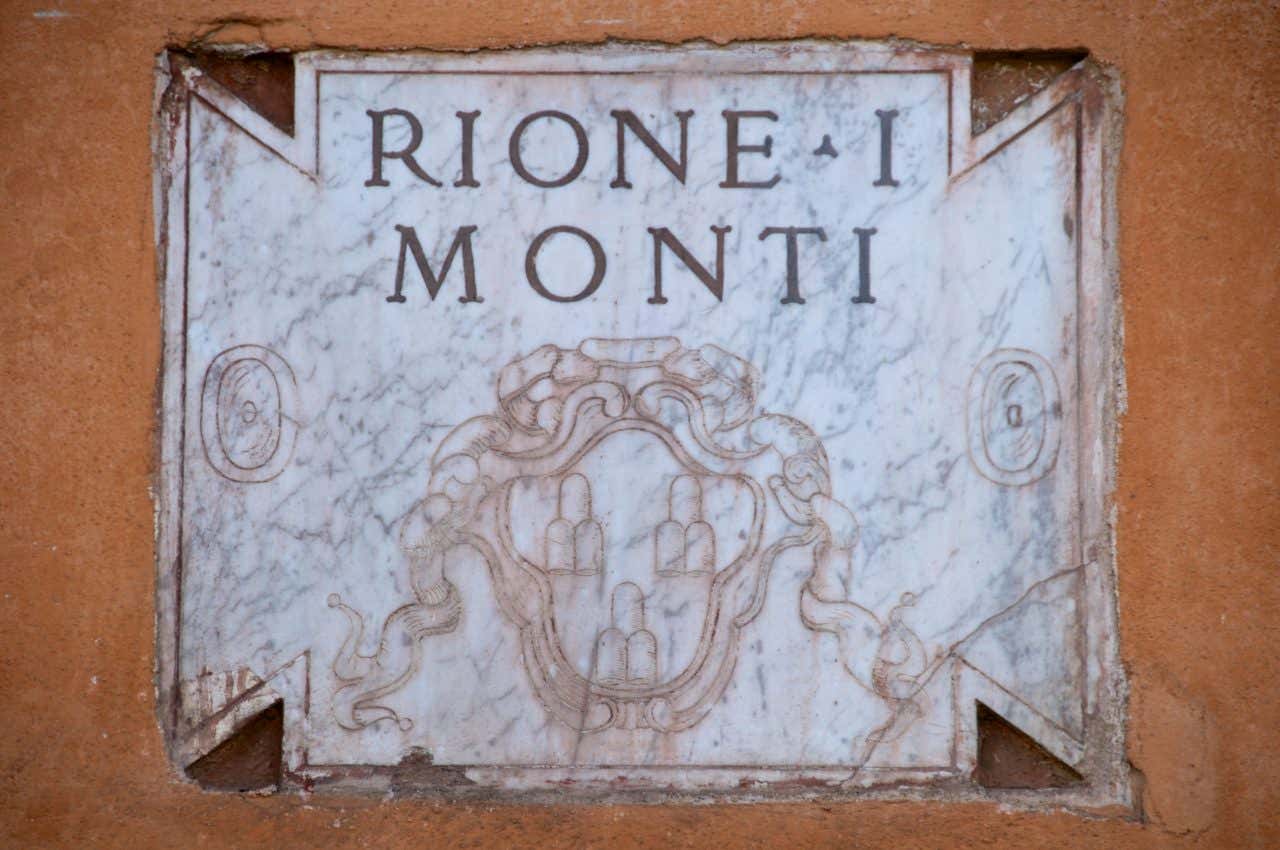 Targa storica in marmo bianco con scritta Rione I Monti e stemma araldico con tre monti sormontati da stella, su muro ocra nel quartiere Monti