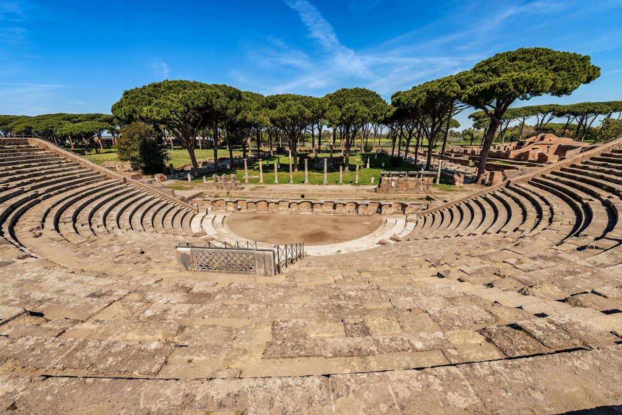 Teatro Romano di Ostia Antica, anfiteatro del I secolo d.C. con cavea semicircolare ben conservata, orchestra centrale e pini domestici caratteristici del parco archeologico sullo sfondo
