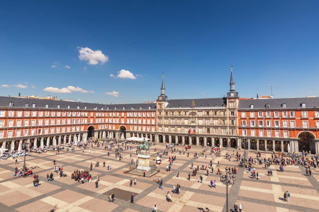 Vue panoramique sur la Plaza Mayor de Madrid entourée de façades orangées et fréquentée par des visiteurs