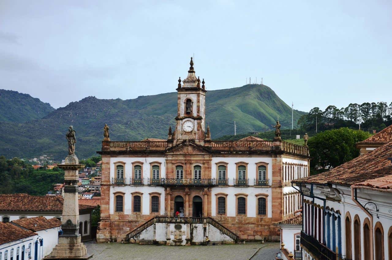Fachada do casarão que abriga o Museu da Inconfidência com a estátua de Tiradentes em primeiro plano e montanhas ao fundo