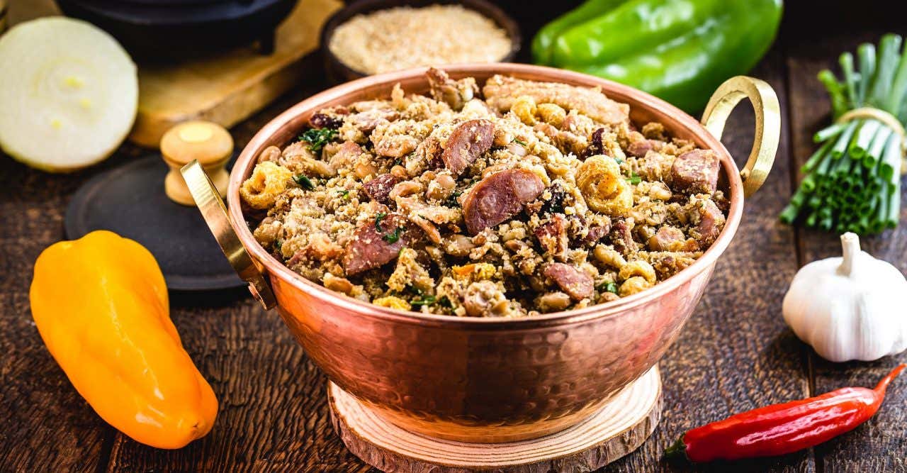 Feijão-tropeiro em panela de cobre, cozinha rústica, com ingredientes e legumes ao fundo