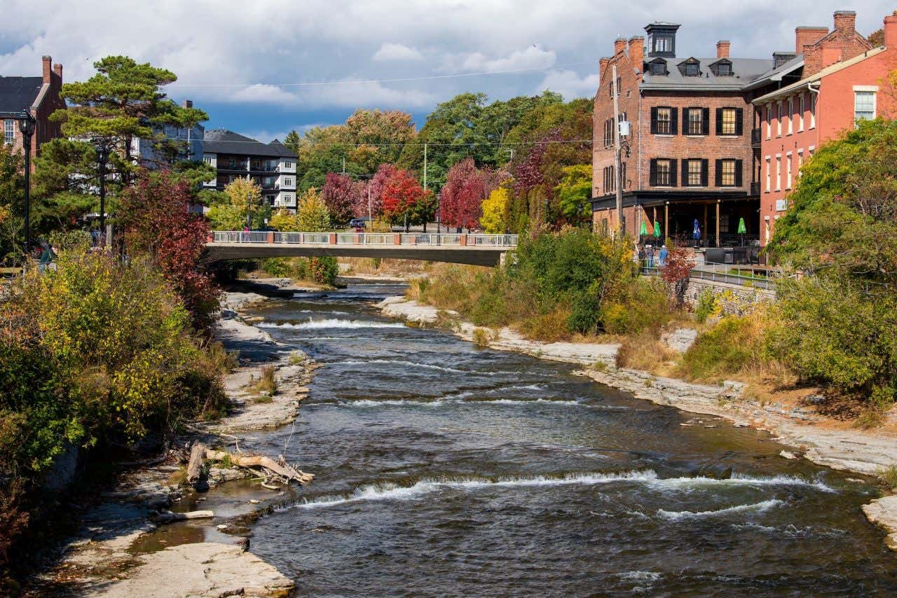 Panorâmica de Port Hope com uma ponte que passa sobre um riacho, construções de tijolo à vista e árvores ao redor, um dos cenários de filmes de terror mais bonitos do Canadá