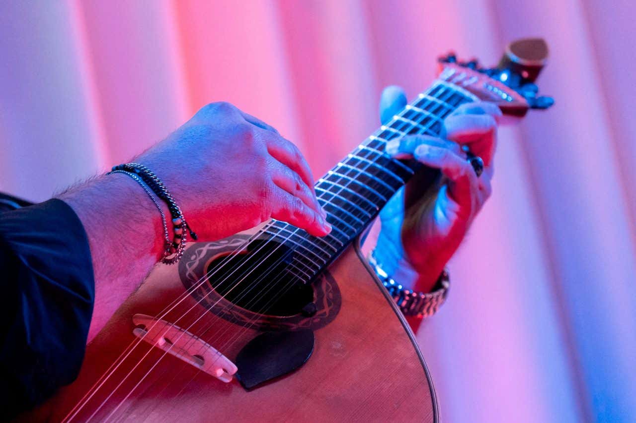 Primo piano su delle mani che suonano una chitarra portoghese illuminata da luci blu e rosse