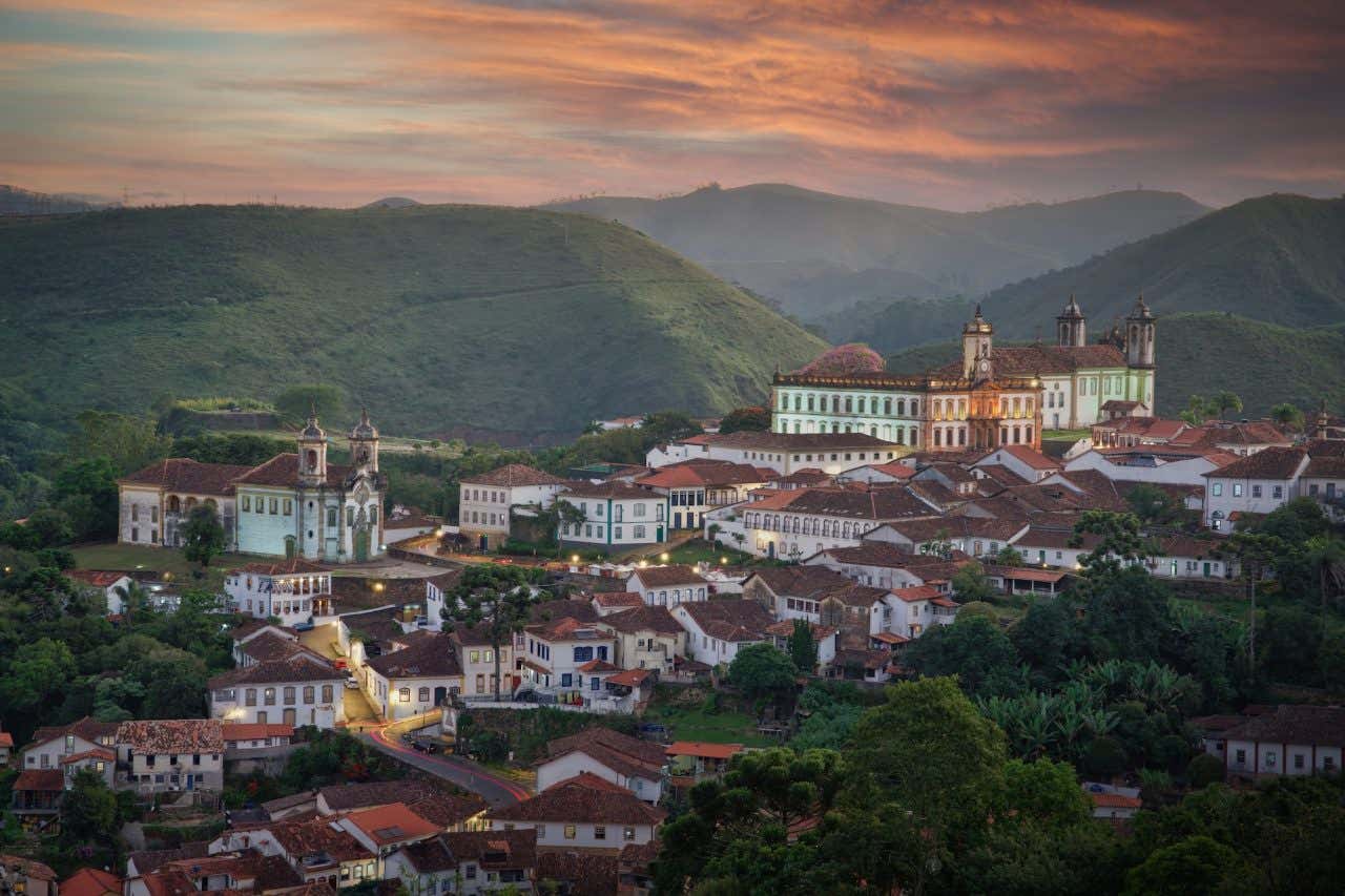 Vista panorâmica de Ouro Preto com diversas casinhas, igrejas e o Museu da Inconfidência, cercada de colinas e natureza