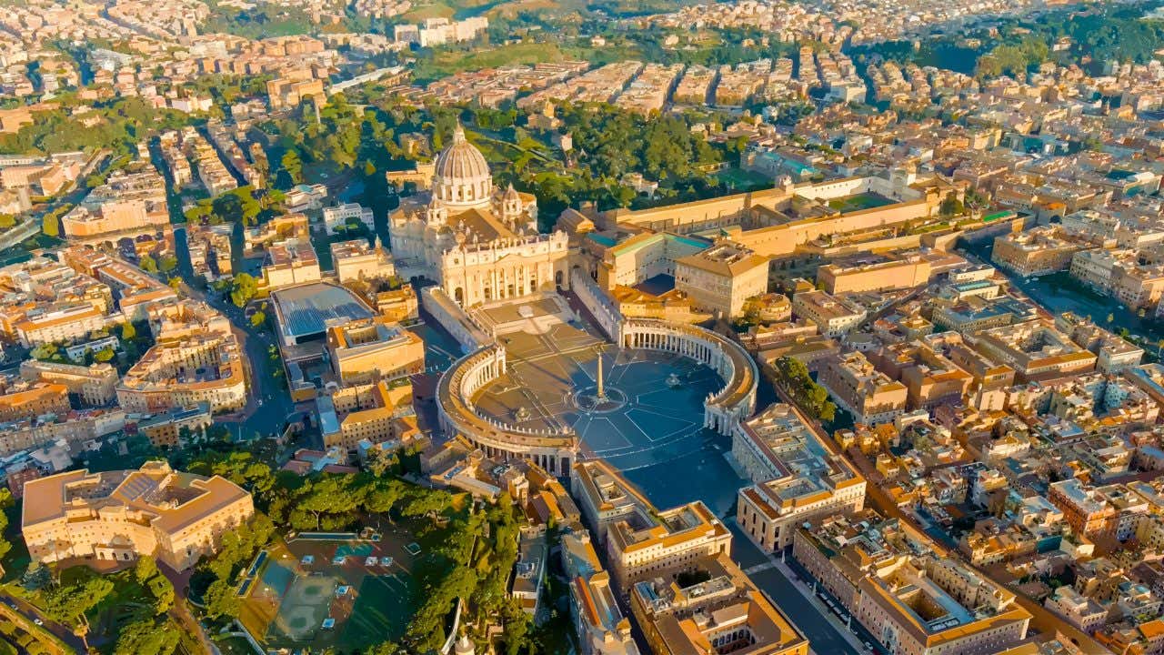 Suggestiva vista aerea della Basilica di San Pietro con la cupola di Michelangelo e il colonnato del Bernini illuminati dalla luce dorata del tramonto, Piazza San Pietro, Città del Vaticano, Roma, Italia