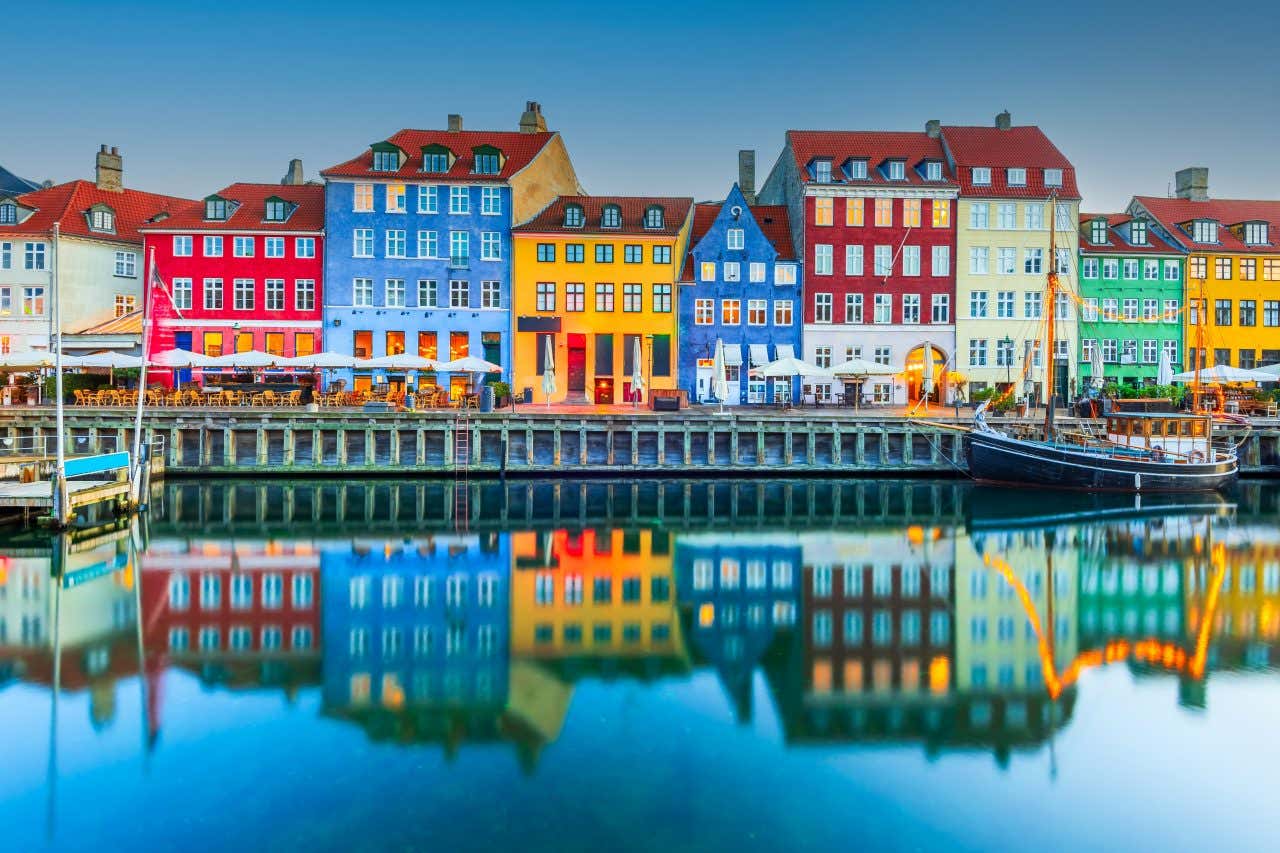 Le case colorate di Copenaghen affacciate su uno dei suoi canali, dove sono attraccate piccole imbarcazioni e un molo in legno che fa capolino sul lato sinistro della foto