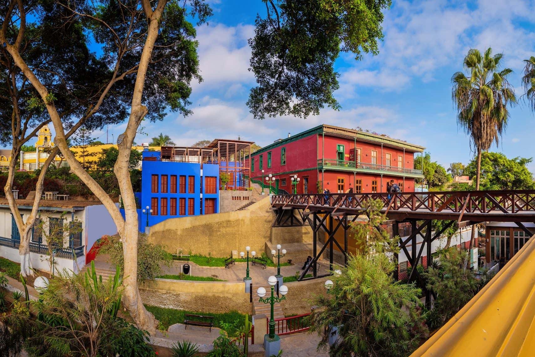 Casas coloridas y un puente de madera, rodeada de árboles y farolas