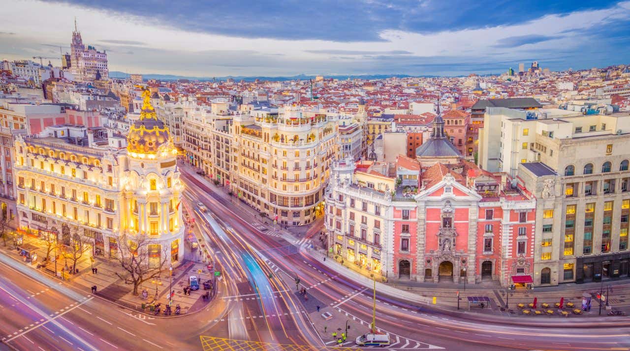 Vista aerea di Gran Vía a Madrid al tramonto con l'edificio Metrópolis illuminato e scie luminose del traffico