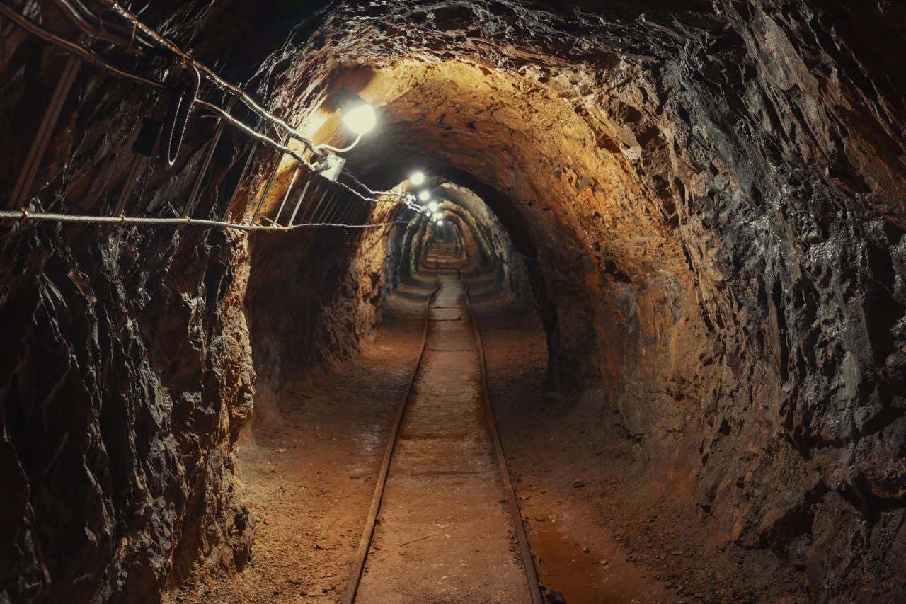 Cabos e trilhos em um túnel subterrâneo com paredes rochosas na Mina da Passaem