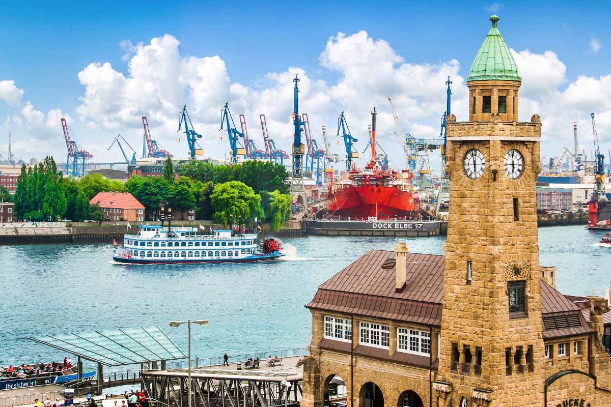 Varias grúas de obras a lo lejos y un barco cruzando un lago junto a un barrio de estética portuaria de Hamburgo