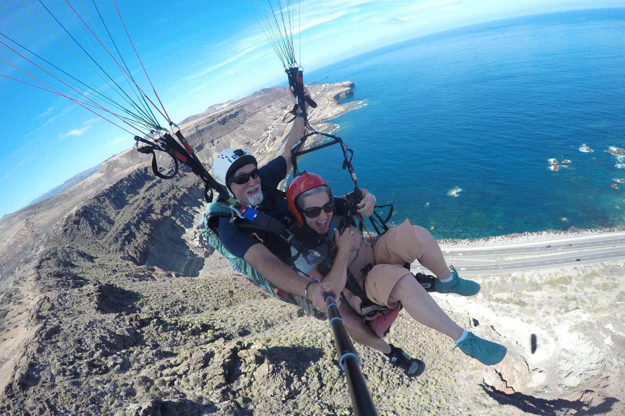 Dos personas, un hombre y una mujer, grabándose con una GoPro durante un vuelo en parapente sobre la playa Las Canteras en Gran Canaria
