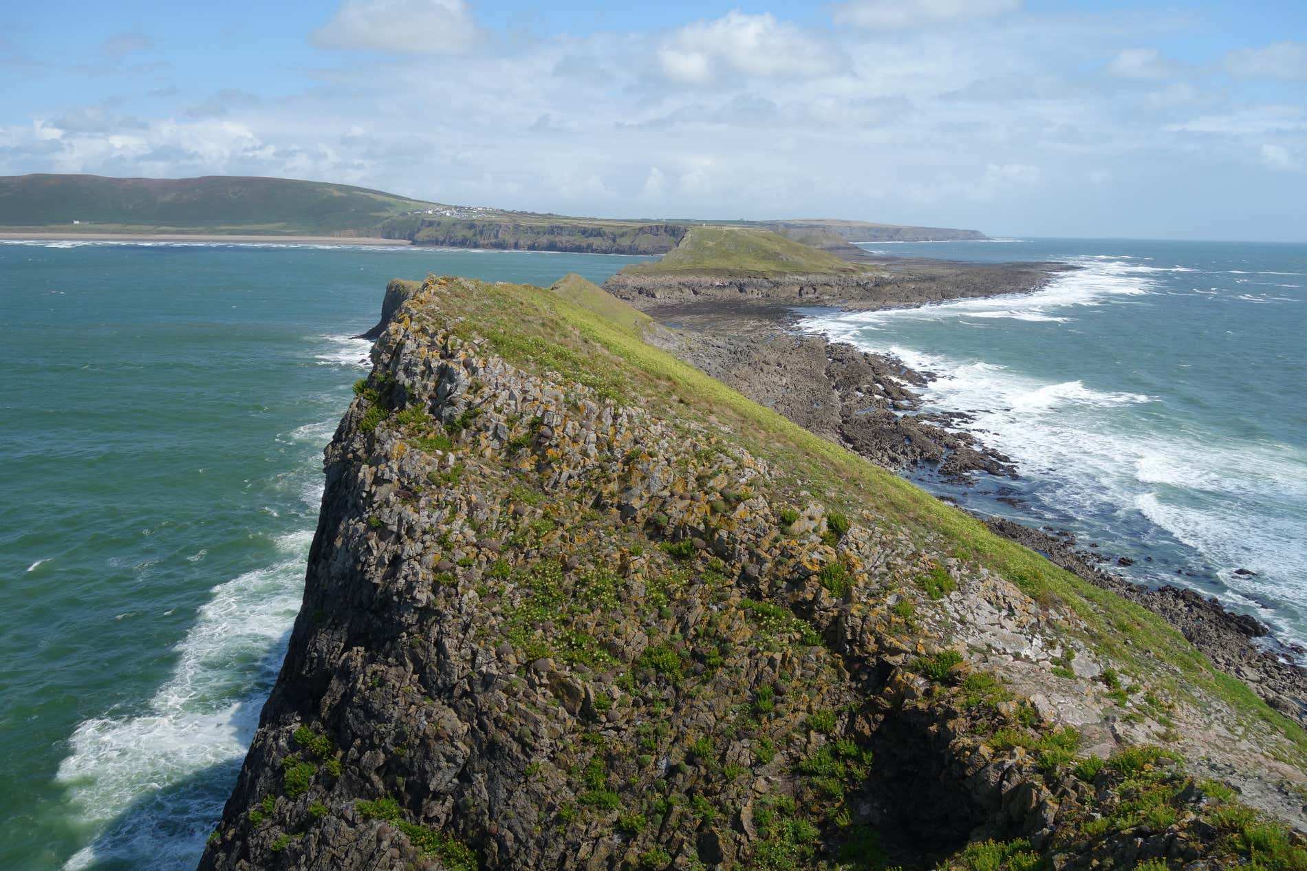 Vista di imponenti scogliere circondate dal mare con una costa sullo sfondo