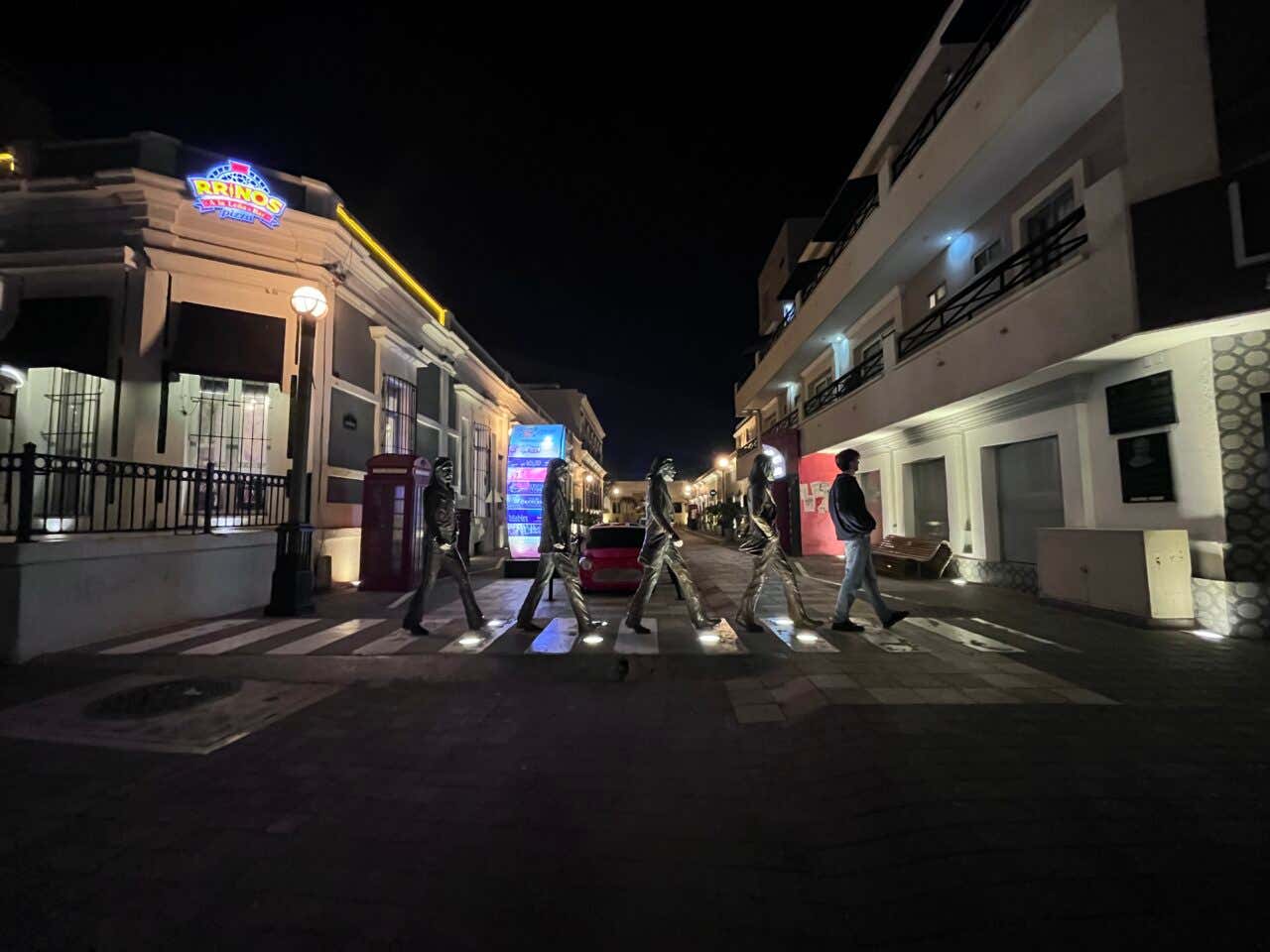 A tourist posing with the Beatles' statues in Mazatlán at night.