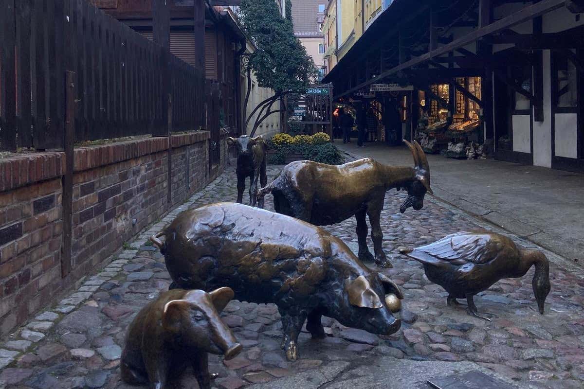 Varias esculturas de bronce de animales como gansos, cabras o cerdos en una calle empedrada con casas tradicionales con soportales de madera