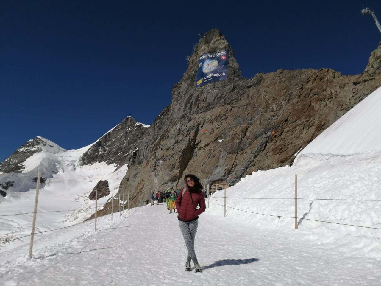 Una mujer sonríe para una foto en un sendero nevado con un pico rocoso al fondo