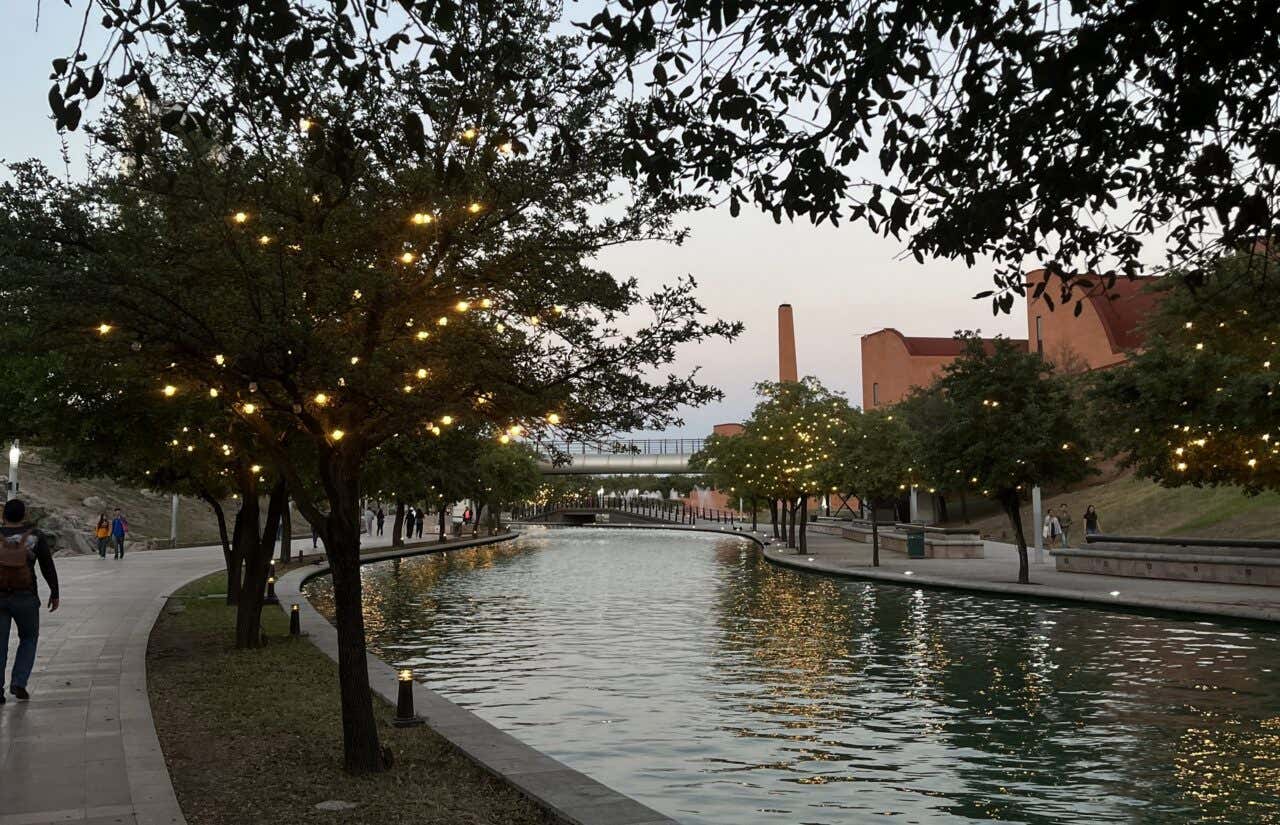 Paseo Santa Lucía in the evening, with lights in the trees, and a clear pinkish sky in the background and people walking along the water's edge.