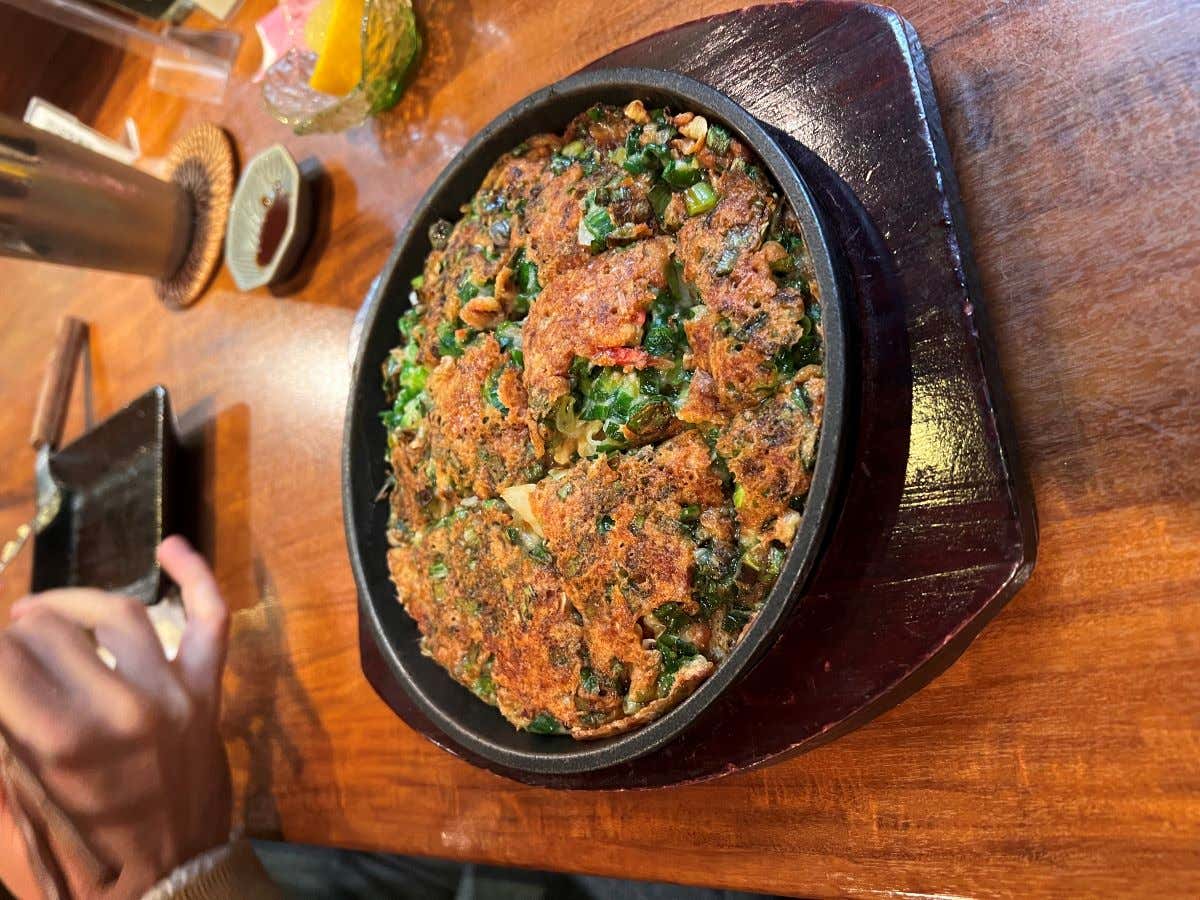 Okonomiyaki sobre un plato de color negro cubierto de varios ingredientes