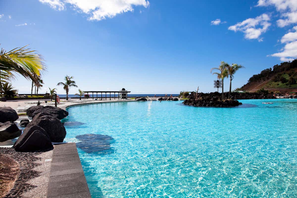 Una piscina de aguas claras ubicada muy cerca del mar y con unas islas artificiales hechas con piedra volcánica
