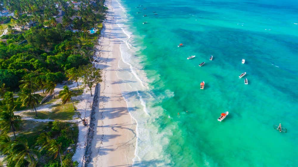 Vista dall'alto del mare turchese leggermente mosso con alcune imbarcazioni nei pressi di una spiaggia selvaggia di sabbia bianca
