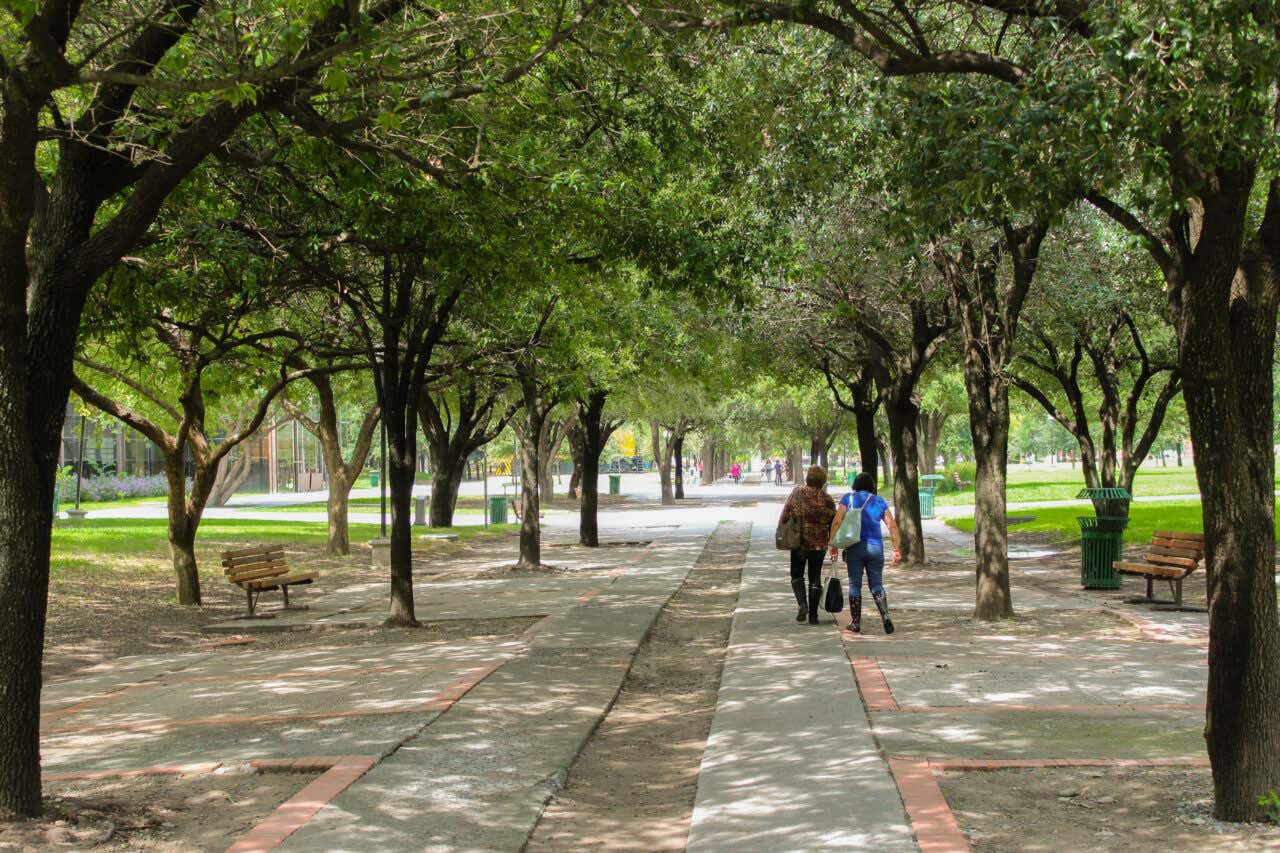 Two people walking in Parque Fundidora with trees all along the pathway.