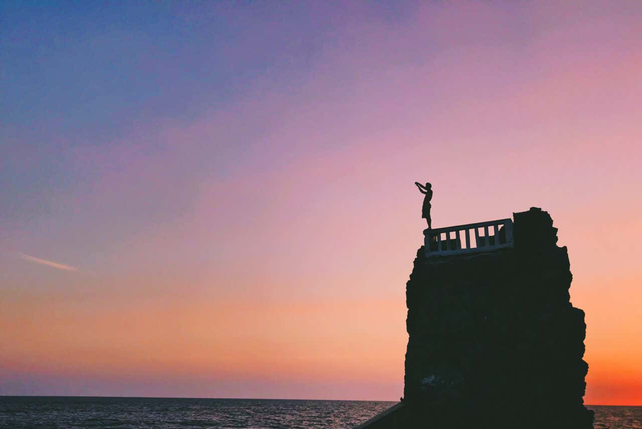 A diver preparing to take the plunge at El Clavadista, with an orange and purple sky in the background.