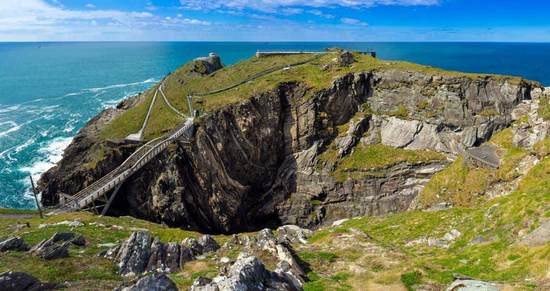 A view of Mizen Head, a cliff with turquoise water beneath it under a blue sky with some white clouds.