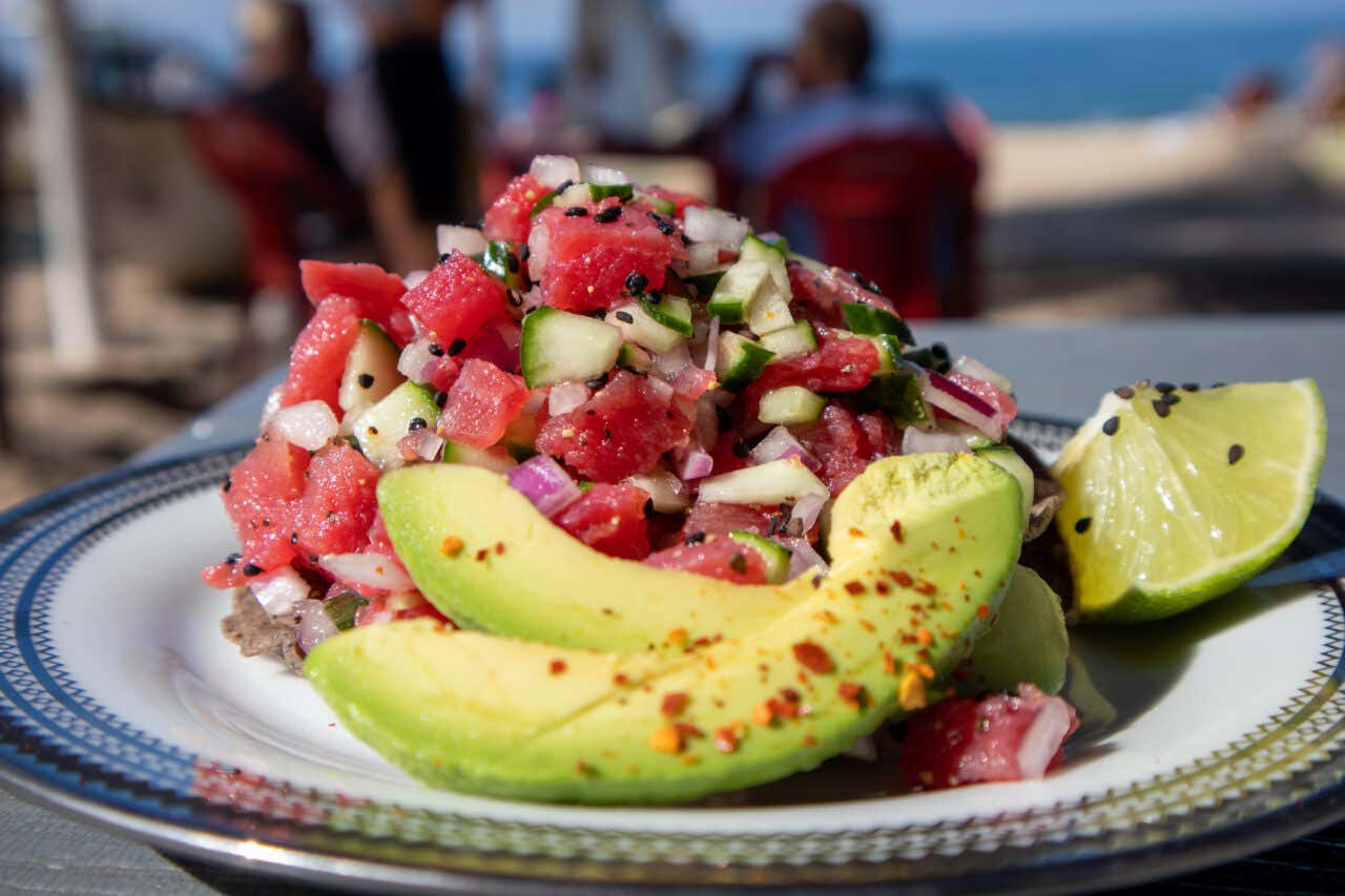 Aguachile made with fresh tuna, avocado, lime, and other vegetables with the beach in the background.