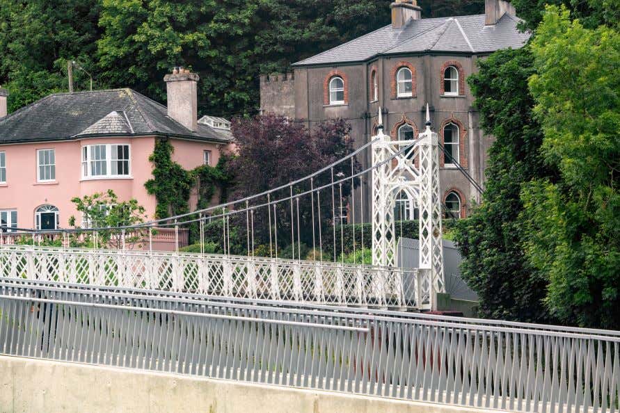 A view of a white pedestrian bridge with houses across the way.