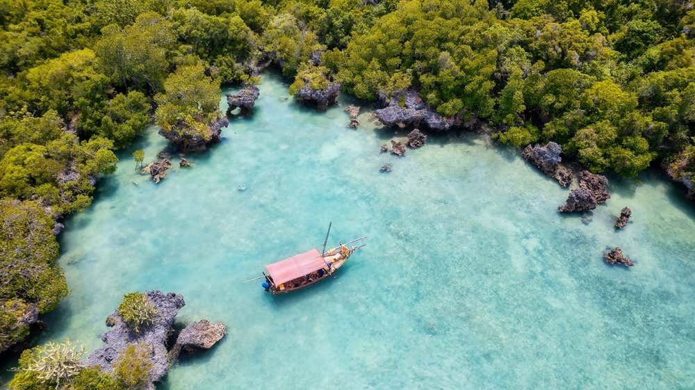 Foto dall'alto di un dhow tradizionale ancorato nel mare cristallino nei pressi di un'isola selvaggia di Zanzibar