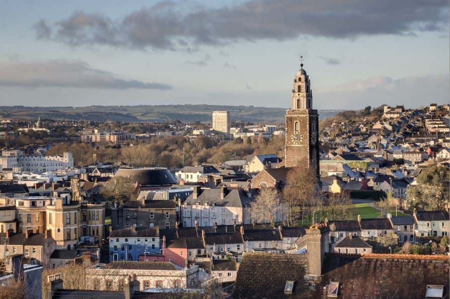 A view of St. Anne's Church towering over Cork City under a cloudy sky.