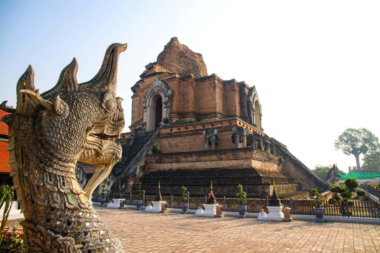 Wat Chedi Luang a Chiang Mai con statua di naga (serpente mitologico) in primo piano e l'antica pagoda parzialmente crollata in mattoni rossi sullo sfondo