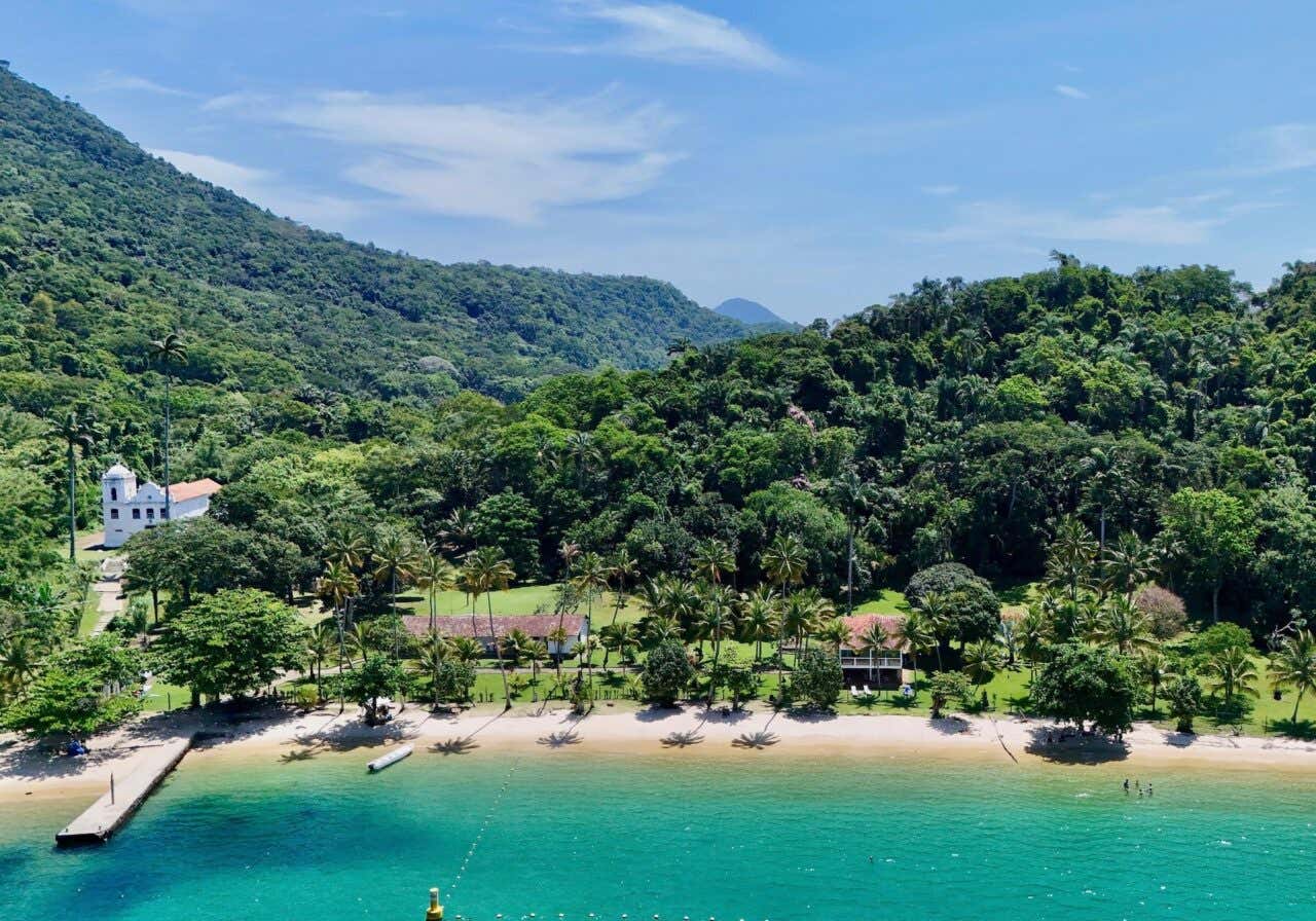 Panorâmica de águas turquesas com frondosa vegetação ao fundo e casas coloniais