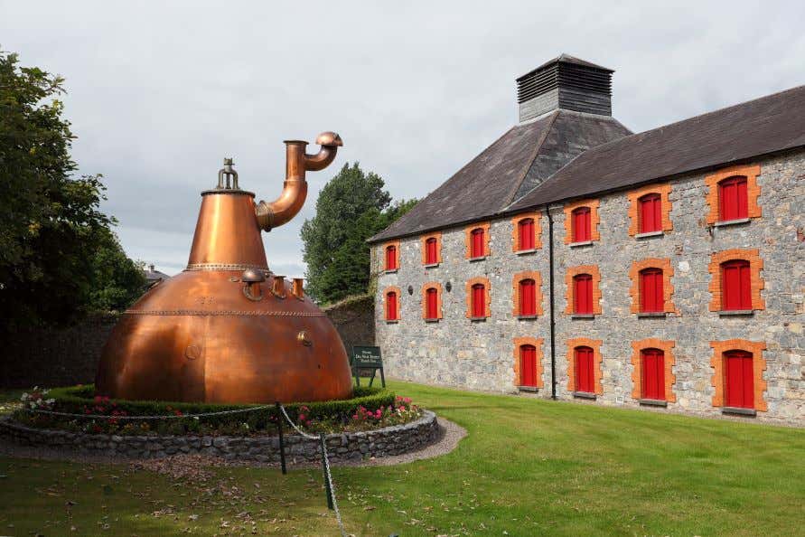 A view of the Jameson Distillery in Midleton with a bronze statue in front of it on the grass.